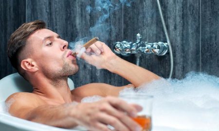 Man drinking whiskey and smoking cigar in bath.