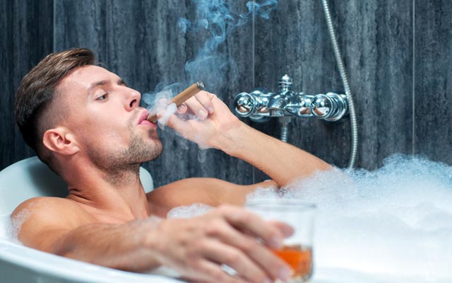 Man drinking whiskey and smoking cigar in bath.