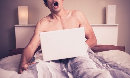 Man using a computer and masturbating in bed