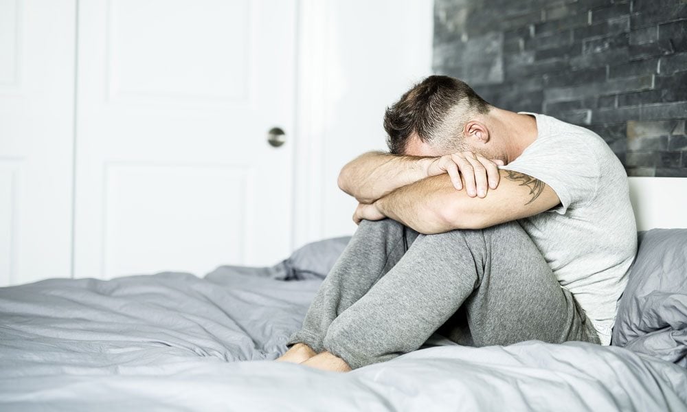 A sad man sitting on a bed.