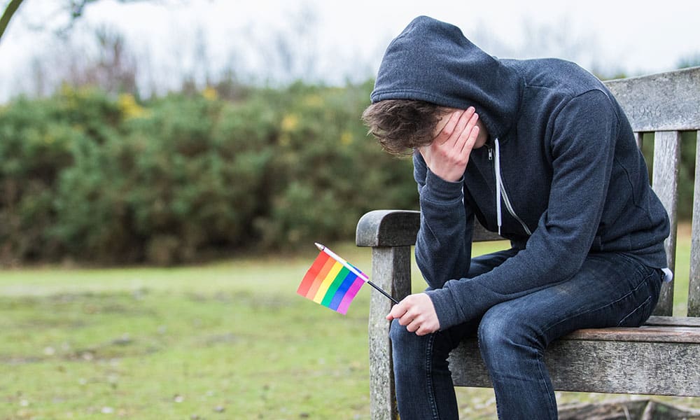 Depressed teenage boy holding a pride flag