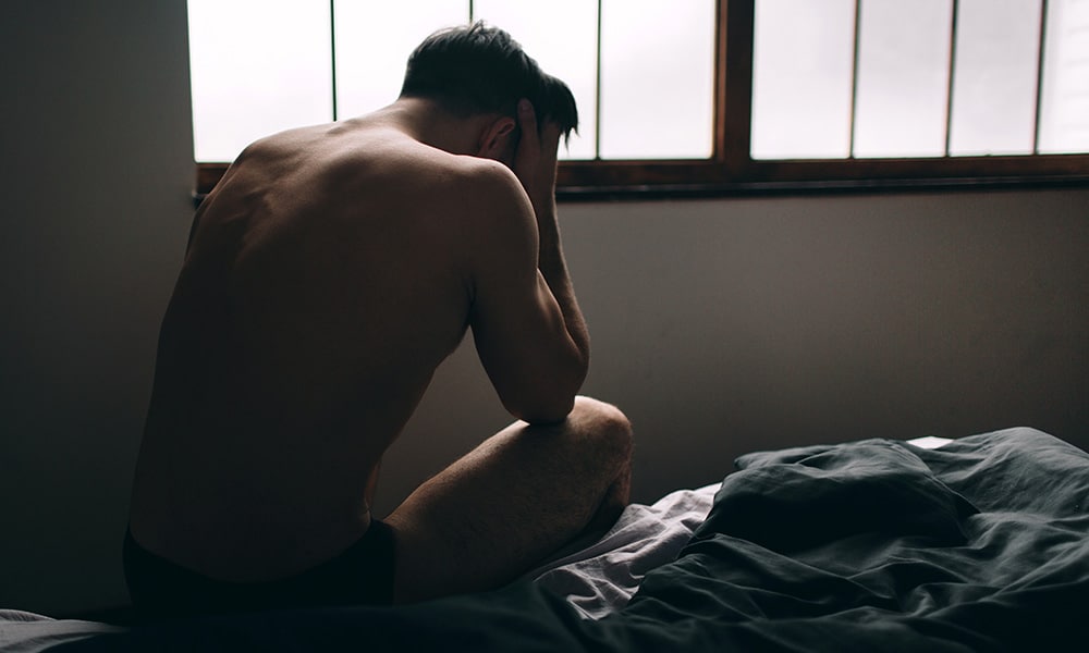 Depressed man sitting on bed in an empty room.