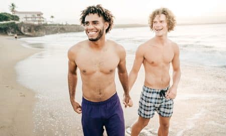Gay couple walks together on a beach.