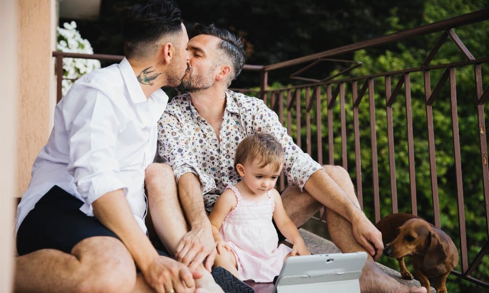Gay couple kissing with daughter and dog on balcony