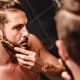 Hipster man focusing on combing beard in front of a mirror