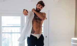 Adult man with tattoos putting on shirt in bedroom