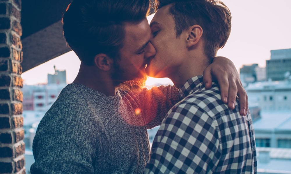 Young gay couple on the balcony enjoying in sunset.