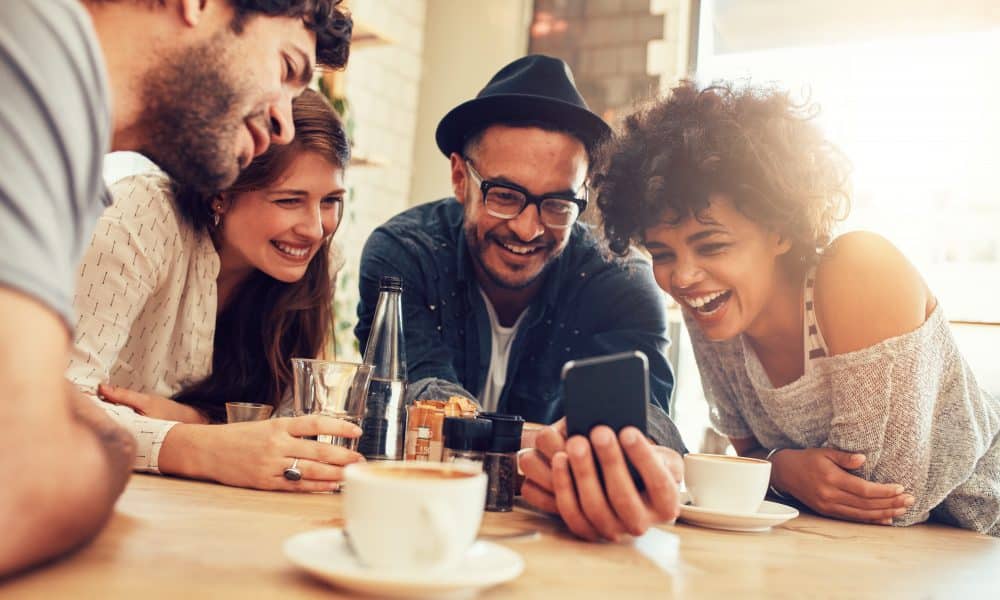 Portrait of cheerful young friends looking at smart phone while sitting in cafe