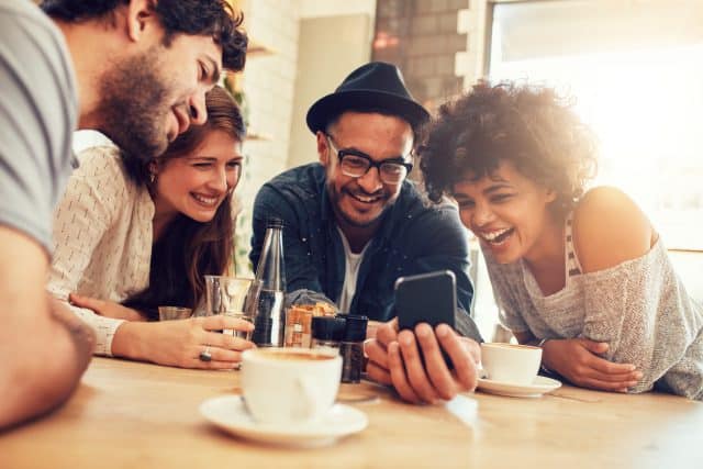 Portrait of cheerful young friends looking at smart phone while sitting in cafe