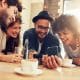 Portrait of cheerful young friends looking at smart phone while sitting in cafe