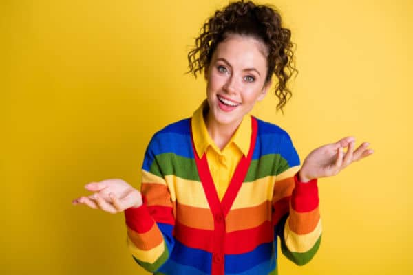 female in rainbow sweater with questioning hands and expression