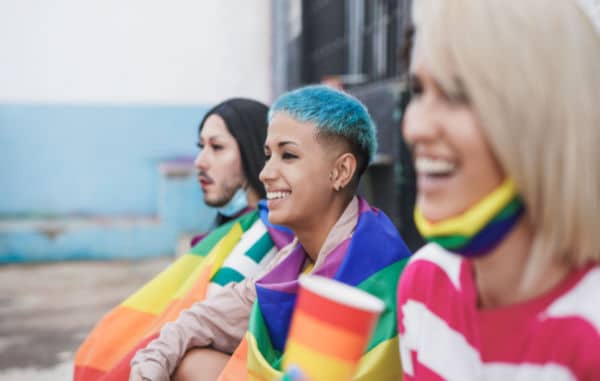 3 youth sitting on curb with rainbow clothing and smiling