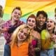 group of seven youth under rainbow flag smiling