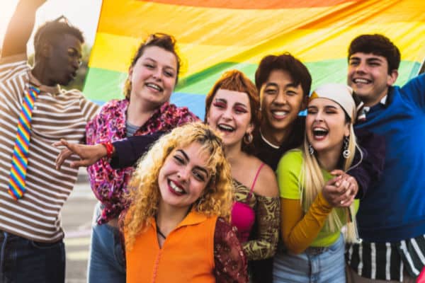 group of seven youth under rainbow flag smiling