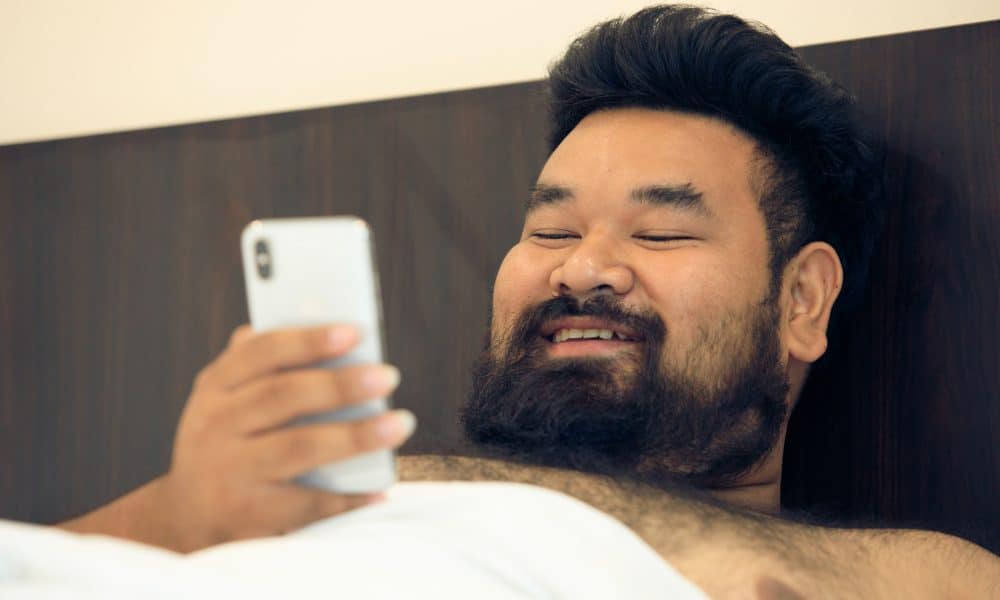 Asian man shirtless with smartphone in bed