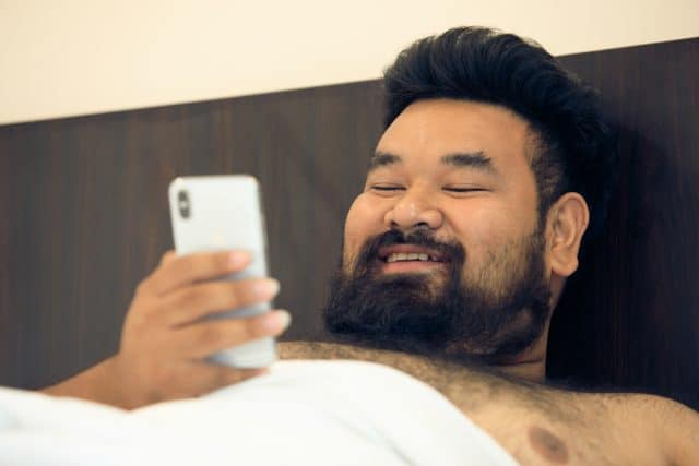 Asian man shirtless with smartphone in bed