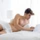 Young shirtless man working on a laptop computer lying in bed during the day