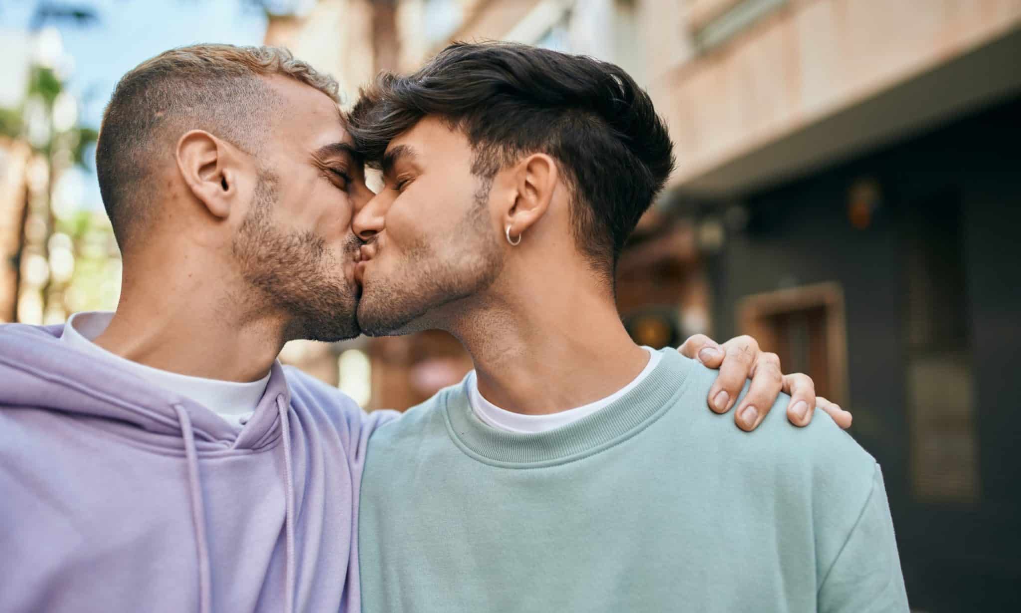 Young gay couple hugging and kissing at the city.