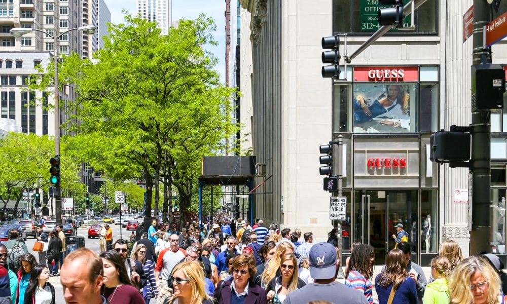 A crowded shopping street with lots of pedestrians, some green trees and Retail-Shops in Chicago.