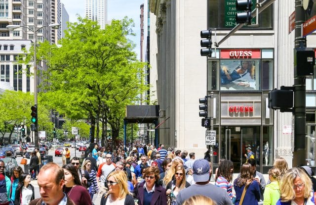A crowded shopping street with lots of pedestrians, some green trees and Retail-Shops in Chicago.