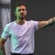 Liam Payne, former One Direction singer, performs on stage wearing a white t-shirt, with his left arm raised and eyes closed. His arm displays several visible tattoos, including a clock on his forearm. The background is a neutral concert setting.