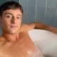 Tom Daley lounging in a bubble-filled bathtub, with a relaxed expression on his face, his right arm resting on the tub's edge.